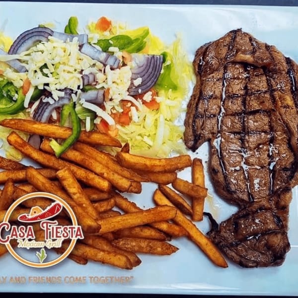 Grilled steak with fries and a side salad topped with cheese, onions, and peppers.