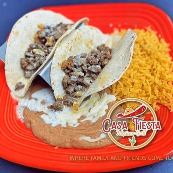 Two beef tacos with melted cheese, refried beans, and yellow rice on a red plate.