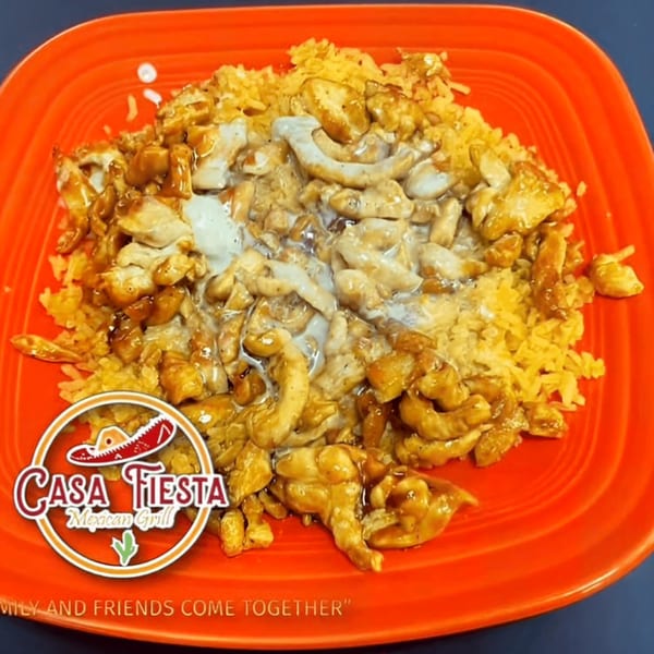 Casa Fiesta Mexican Grill's chicken and rice dish, topped with a creamy sauce, on an orange plate.