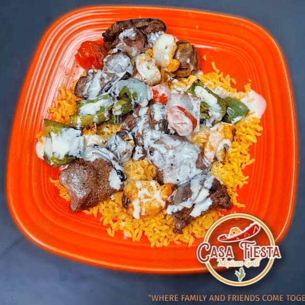 Casa Fiesta's Mexican dish with meat, vegetables, and rice, drizzled with white sauce on an orange plate.