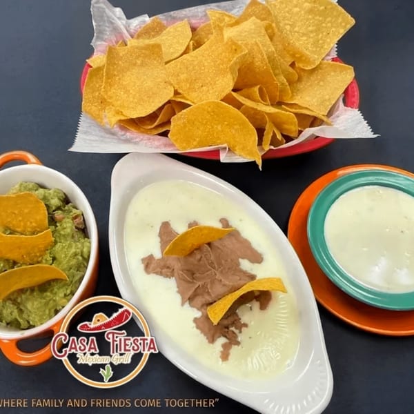 A basket of tortilla chips, guacamole, queso with refried beans, and a side of queso.